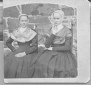 SA0002 - Sadie Neale on right, Emma Neale on left. Both are seated on chairs outside. Photo shows a stone wall behind them. Caption on the back.